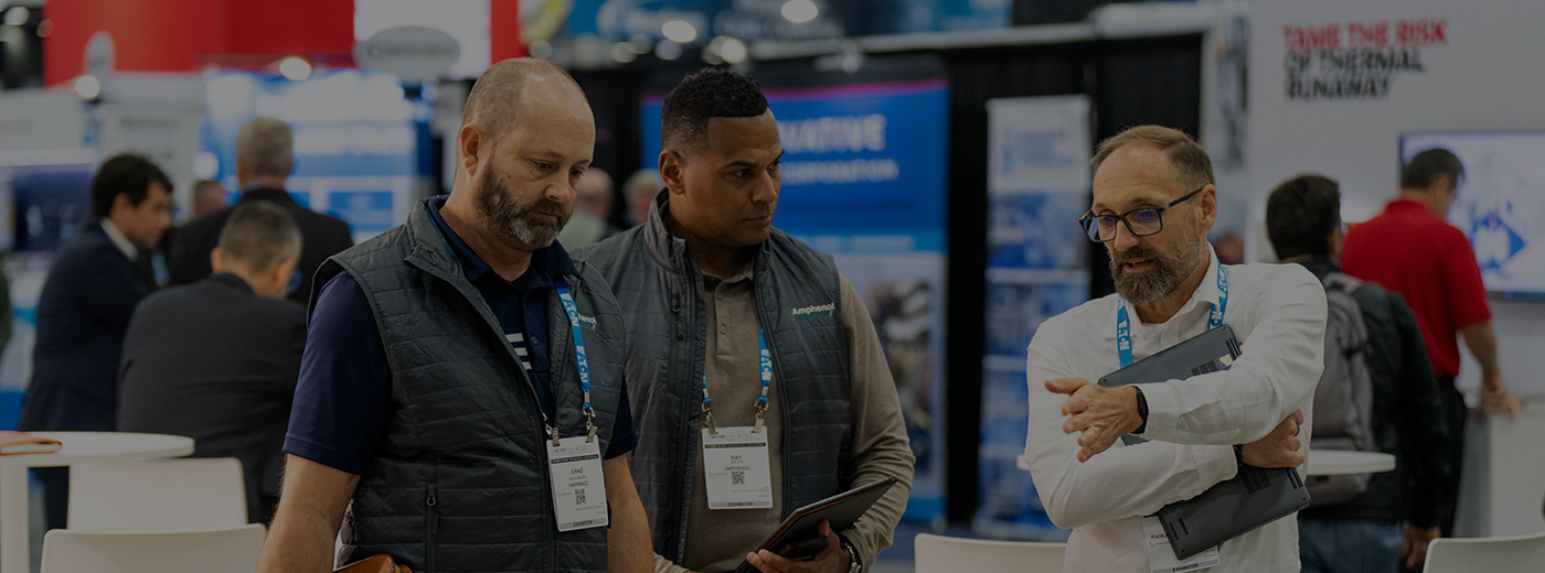 A diverse group of people networking and discussing around booths at a bustling trade show event